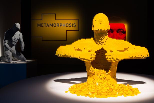 Eine Ausstellung mit zwei menschlichen Figuren aus Legosteinen, die „Metamorphose“ darstellen.