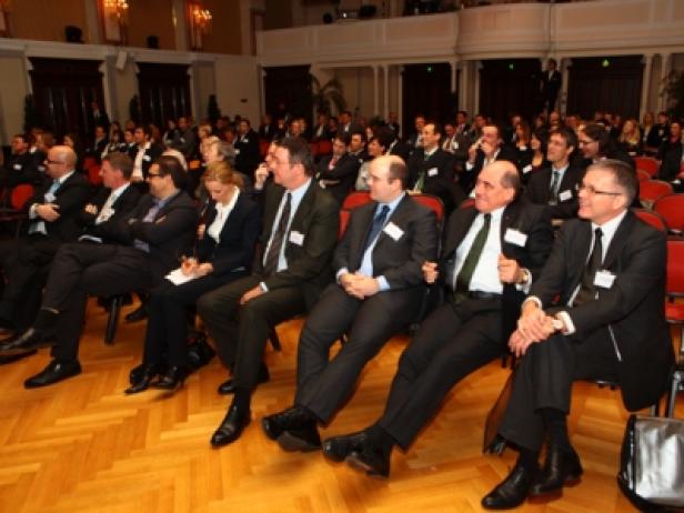 Zuschauer sitzen in Anzügen bei einer Konferenz oder einer ähnlichen Veranstaltung.