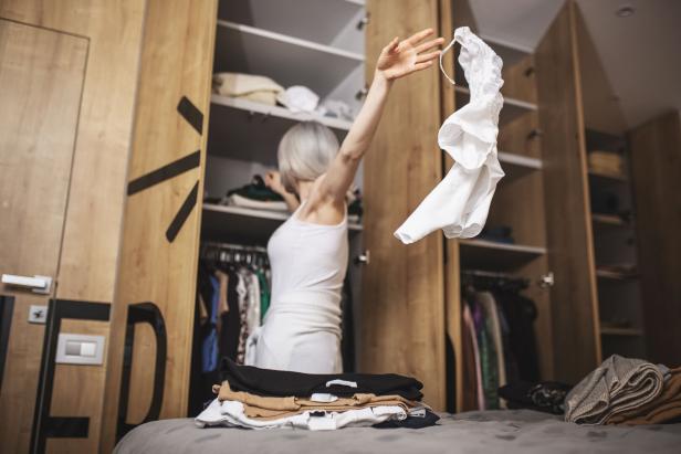 Eine Frau wirft ein weißes Kleidungsstück vor einem offenen Kleiderschrank in die Luft.