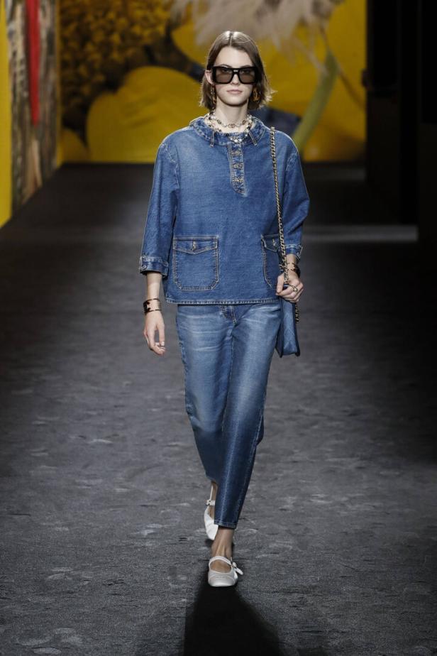 Eine Frau in einem Jeans-Outfit und Sonnenbrille läuft auf einem Laufsteg.