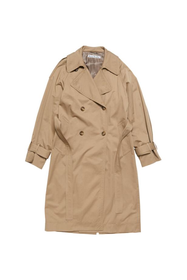 Ein beiger Trenchcoat der Marke Acne Studios vor einem weißen Hintergrund.