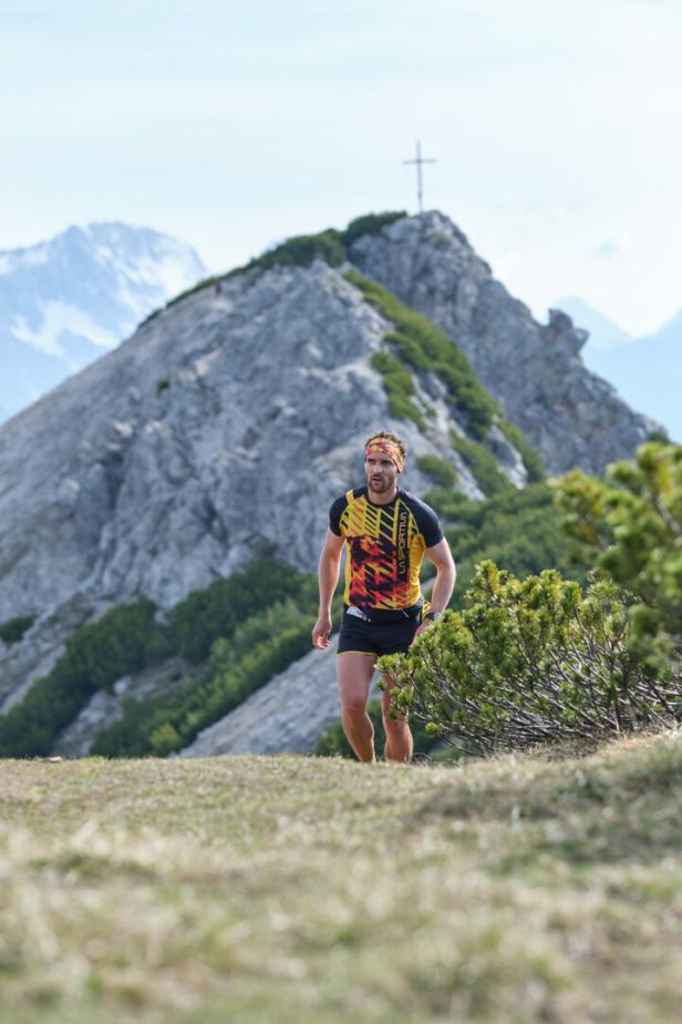 Mann beim Trailrunning im Sommer in den Tiroler Bergen bei Imst, Gipfelkreuz im Hintergrund