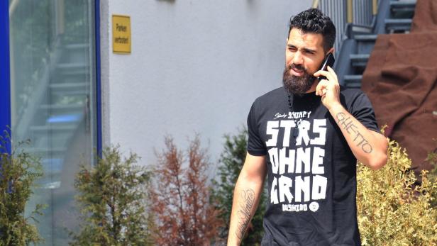 Bushido telefoniert im Freien mit seinem Handy.