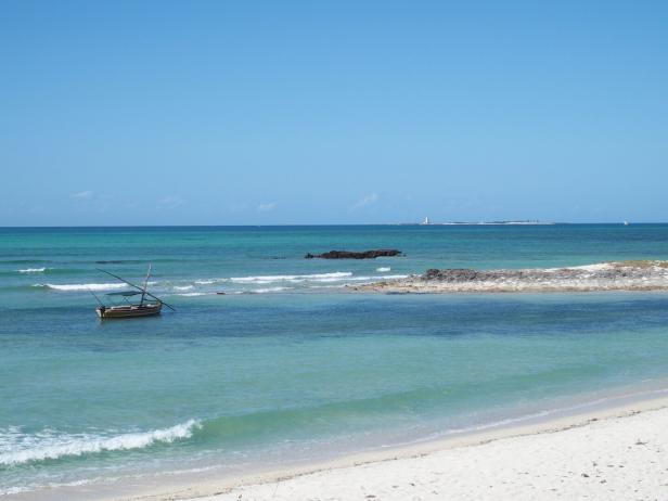 Türkises Wasser an einem Sandtrand in Mosambik, kleines Holzboot im Wasser