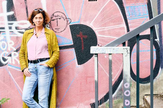 Eine Frau mit Jeans und langem Hemd posiert vor einer Graffiti-Wand.