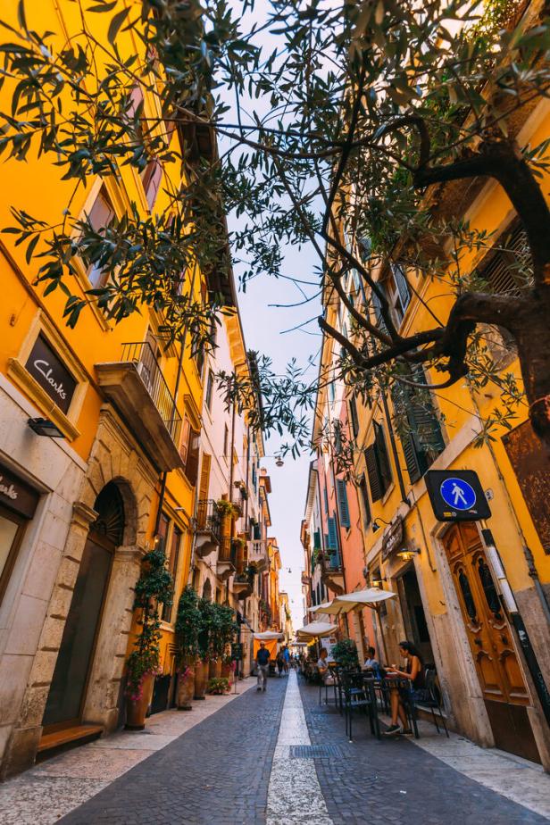 Eine belebte Gasse mit Cafés und Geschäften in einer italienischen Stadt.