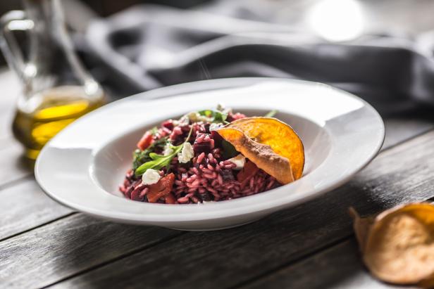Ein Teller mit rotem Risotto, garniert mit Ziegenkäse und einer Orangenscheibe.
