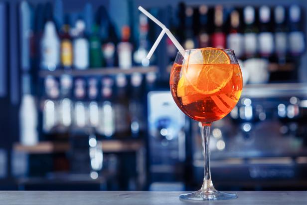 Ein Aperol-Cocktail mit einer Orangenscheibe und einem Strohhalm an einer Bar.