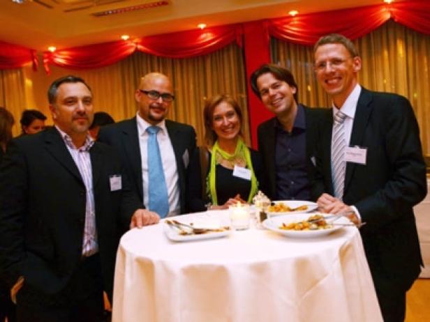 Fünf Personen stehen an einem Stehtisch bei einer Veranstaltung.