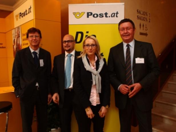 Vier Personen posieren vor einem „Post.at“-Banner.