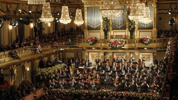 Ein Orchester spielt in einem opulenten Konzertsaal vor Publikum.