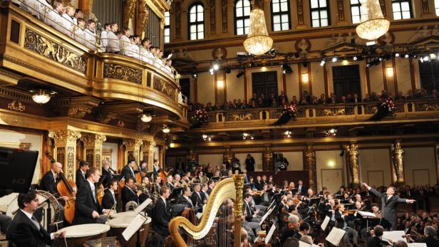 Ein Orchester spielt in einem prunkvollen Konzertsaal mit goldenen Verzierungen.