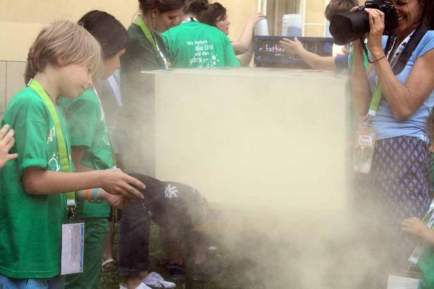 Kinder experimentieren mit Trockeneis, während eine Frau Fotos macht.