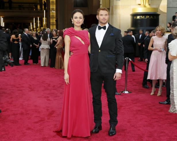 Ein Mann im Anzug und eine Frau in einem roten Kleid posieren auf einem roten Teppich.