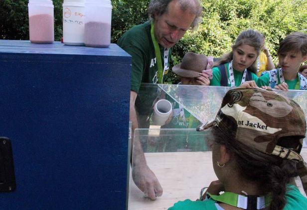 Kinder beobachten ein Experiment mit Sand und einem durchsichtigen Behälter.