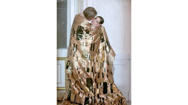 Ein Paar umarmt sich, gehüllt in ein Tuch, das an Gustav Klimts „Der Kuss“ erinnert.