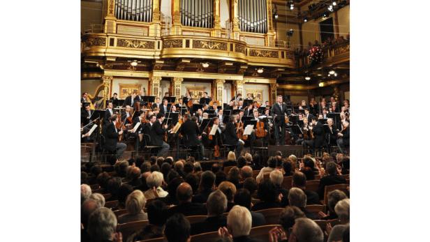 Ein Orchester spielt vor Publikum in einem goldenen Konzertsaal.