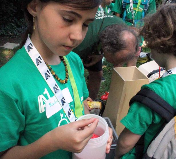 Ein Mädchen im grünen T-Shirt hält eine Dose mit rotem Inhalt in der Hand.