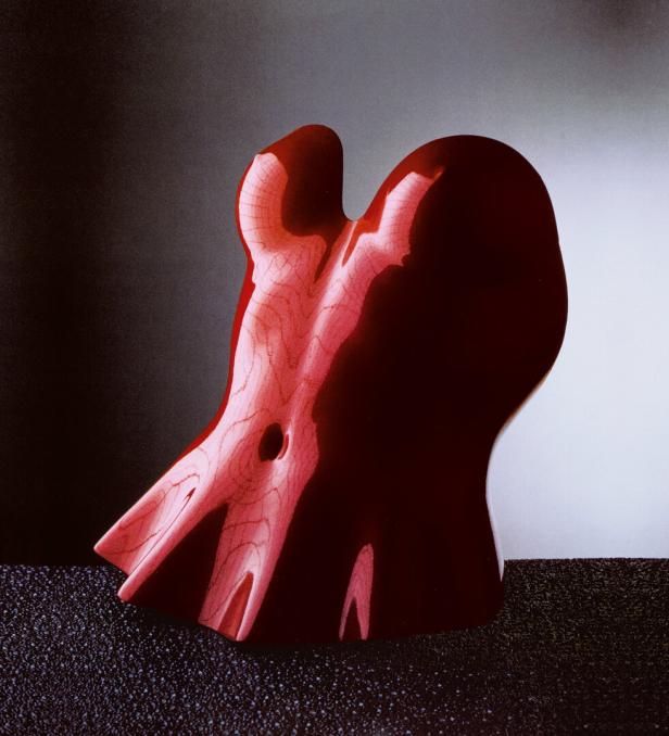 Eine abstrakte, rot lackierte Holzskulptur auf einem dunklen Untergrund.