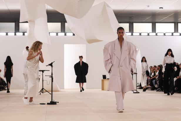 Eine Modenschau mit Models und einer Flötistin in einem minimalistischen, hellen Raum.