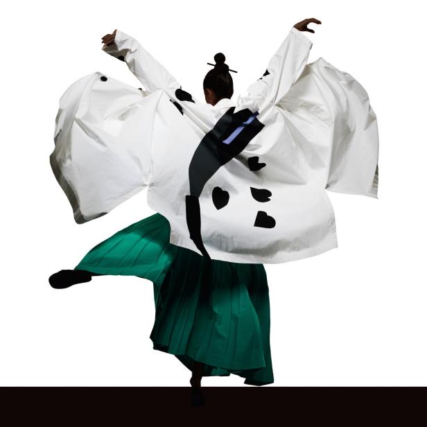 Eine Person in einem weißen Kimono mit schwarzen Herzapplikationen und einem grünen Rock tanzt.