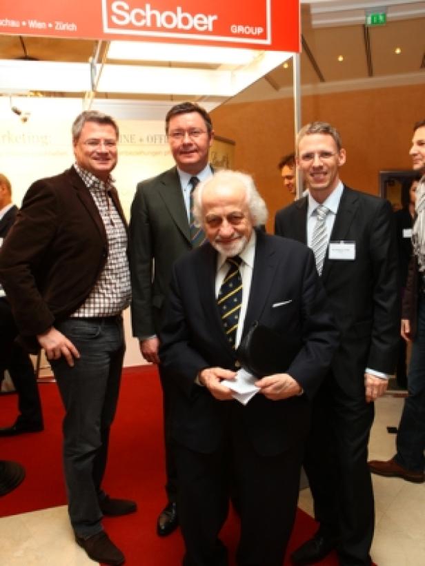 Eine Gruppe von Männern posiert vor einem Stand der Schober Group.