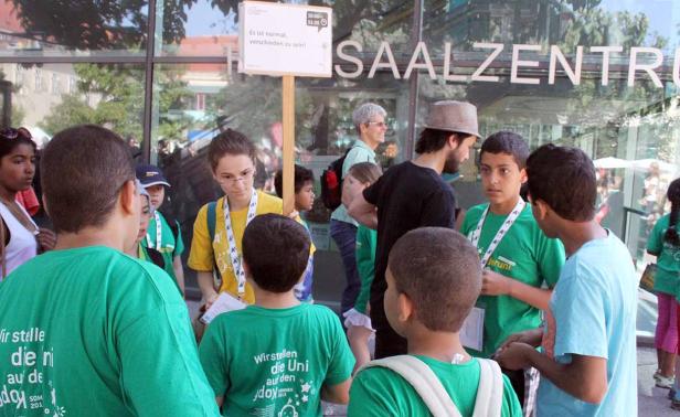 Eine Gruppe von Kindern steht vor dem Saalezentrum mit einem Schild „Es ist normal, verschieden zu sein!“.
