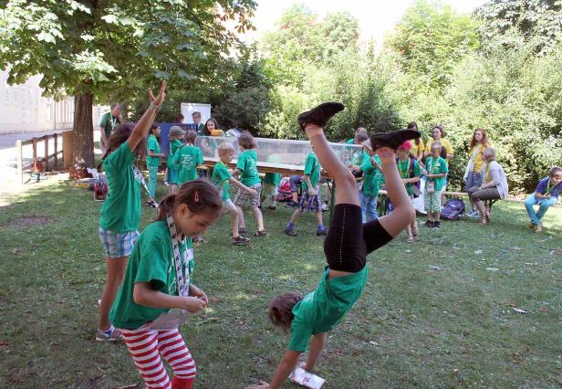 Eine Gruppe Kinder in grünen T-Shirts spielt im Freien, ein Mädchen macht einen Handstand.