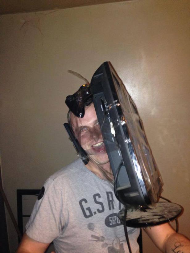 Ein Mann trägt einen alten, staubigen Fernseher als Helm und grinst in die Kamera.