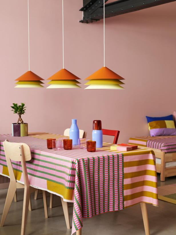 Ein Esstisch mit gestreifter Tischdecke und drei orangefarbenen Hängelampen darüber.