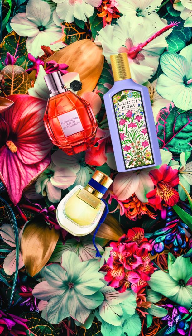 Drei Parfümflaschen von Gucci, Viktor&Rolf und Nomade liegen zwischen üppigen Blumen.