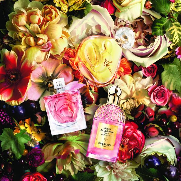 Verschiedene Parfümflaschen liegen zwischen Blumen und Früchten.