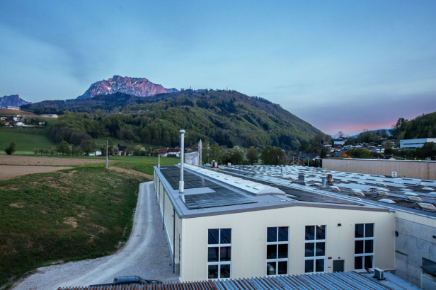 Ein Industriegebäude mit Solaranlagen vor einer Hügellandschaft bei Dämmerung.