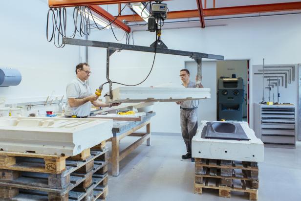 Zwei Männer arbeiten in einer Werkstatt an großen, weißen Formteilen.