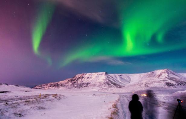 Grüne Nordlichter erhellen den Himmel über einer verschneiten isländischen Landschaft.