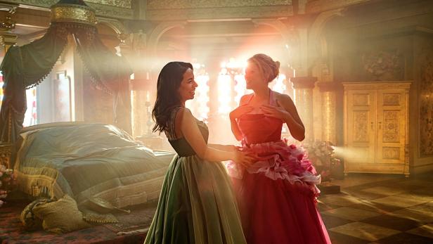 Zwei Frauen in Ballkleidern stehen in einem opulenten Schlafzimmer.