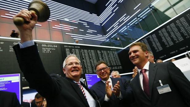 Männer läuten die Börsenglocke vor einer Anzeigetafel.