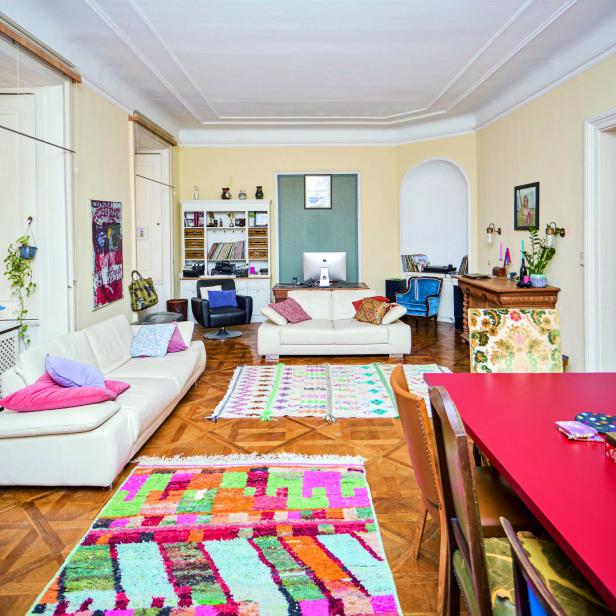 Ein Wohnzimmer mit weißen Sofas, bunten Teppichen und einem roten Esstisch.