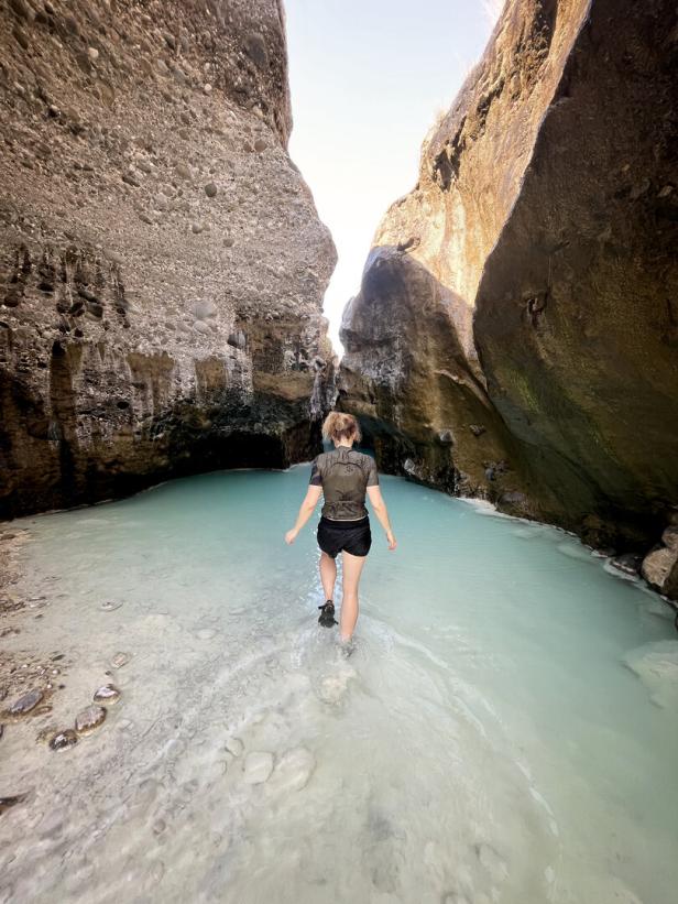 Eine Frau watet durch das türkisfarbene Wasser eines Wadi im Oman.