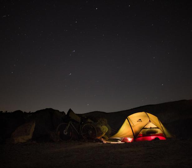 Ein gelbes Zelt und ein Fahrrad unter dem Sternenhimmel im Oman.
