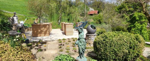 Eine Statue steht in einem Garten mit Hochbeeten und üppiger Vegetation.