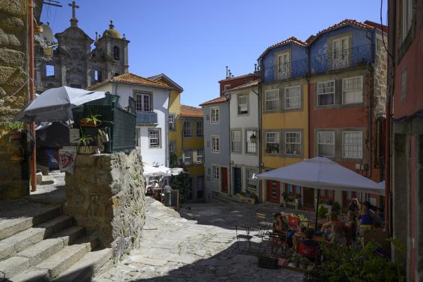 Straßencafe im Altstadtviertel von Porto, Kopfsteinpflaster, draußen stehen Tische mit Schirmen, kleine bunte Häuser, im Hintergrund eine kleine Kirche