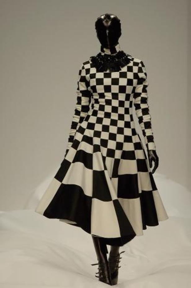 Eine Schaufensterpuppe trägt ein schwarz-weiß kariertes Kleid mit passenden Stiefeln und Handschuhen.