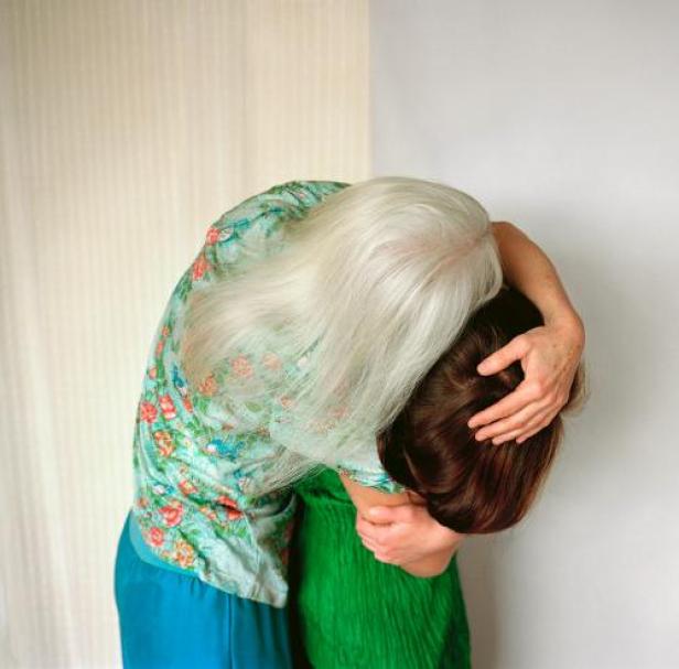 Eine ältere Frau mit grauem Haar umarmt eine jüngere Frau.