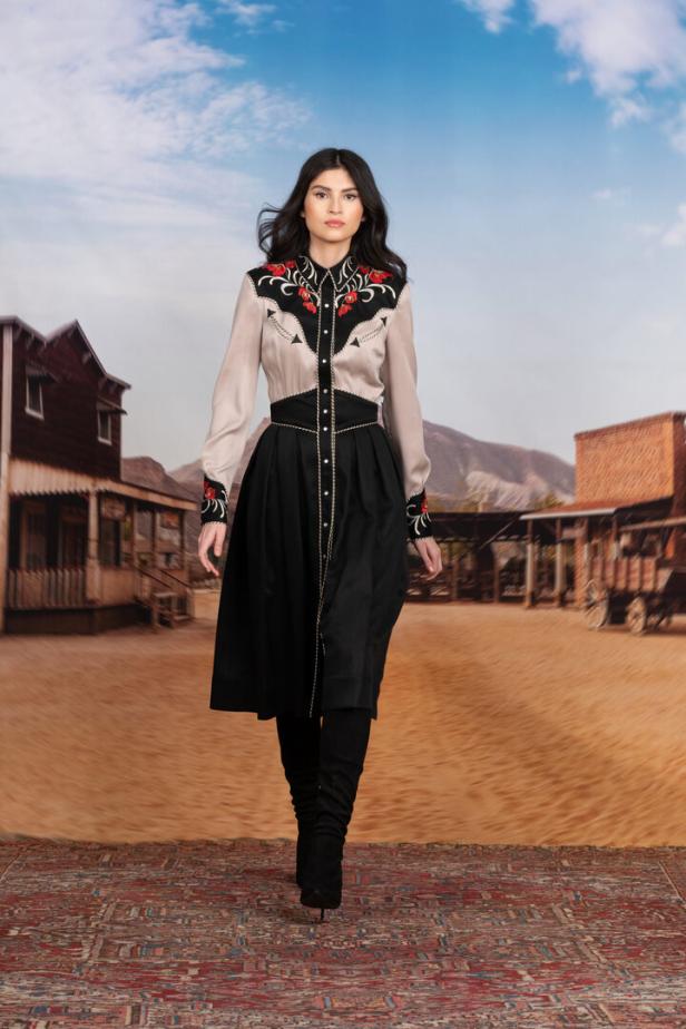 Eine Frau in einem Western-Outfit steht vor einer Kulisse einer Westernstadt.