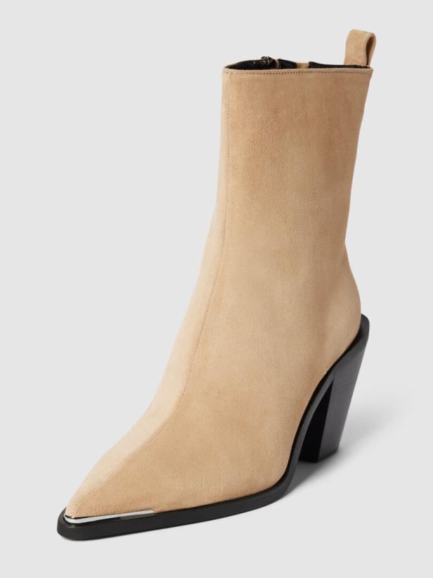 Ein beiger Wildlederstiefel mit spitzer, metallverzierter Zehe und schwarzem Absatz.