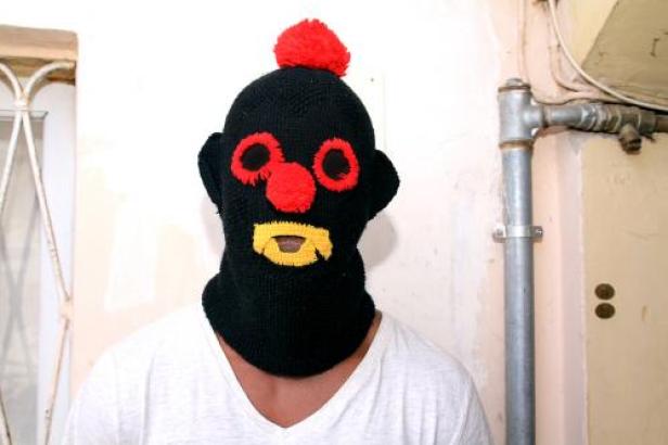 Eine Person trägt eine schwarze, gestrickte Sturmhaube mit roten und gelben Applikationen.