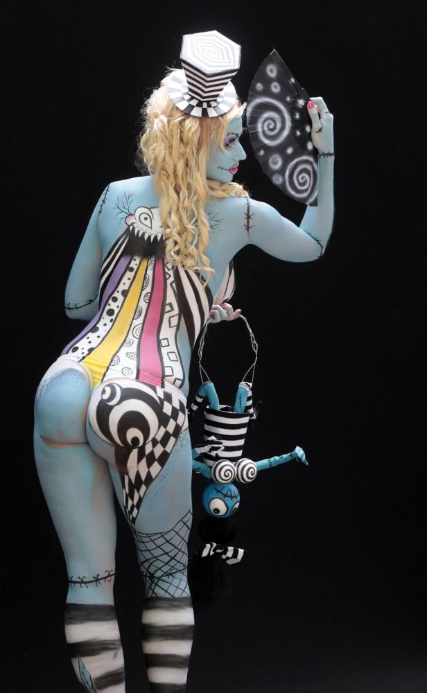 Eine Frau mit Körperbemalung im Stil von „Nightmare Before Christmas“ hält einen Fächer und eine Puppe.