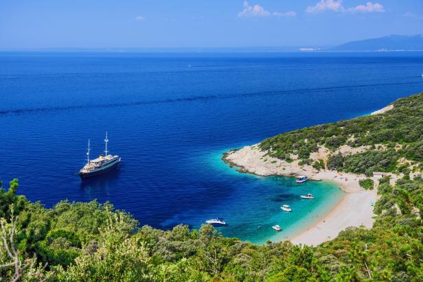 Ein Segelschiff ankert in der Nähe einer malerischen Bucht mit türkisfarbenem Wasser.