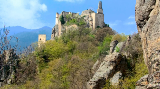 Die Ruine einer mittelalterlichen Burg thront auf einem bewaldeten Hügel.